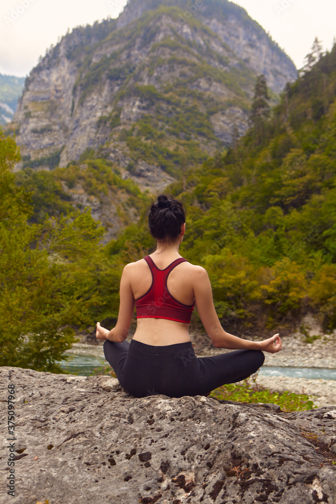 Naklejka premium Yoga classes in nature. The concept of playing sports alone. Social exclusion. A woman does yoga on rocks, near a mountain river flows