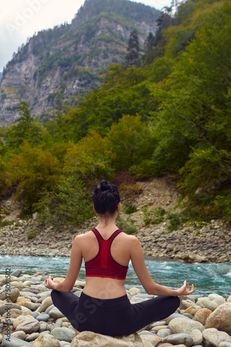 Yoga classes in nature. The concept of playing sports alone. Social exclusion. A woman does yoga on rocks  near a mountain river flows