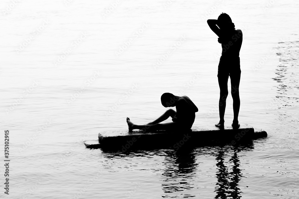 Two boys are bathing on river water and having fun. Image of against sunlight. Silhouette image.