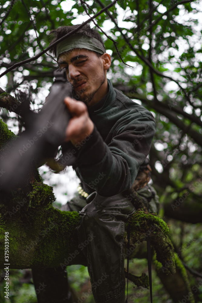 Soldier or revolutionary member or hunter in camouflage on the tree aiming the gun in his hand, hunter concept