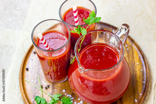 Top view of fresh red tomato juice in a glass with a straw and jar on light wooden background.