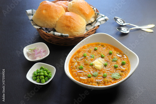 Indian Mumbai Street style Pav Bhaji, garnished with peas, raw onions, coriander, and Butter. Spicy thick curry made of out mixed vegetables served with paav over black background with copy space. 