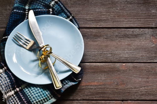 Table setting with cutlery and empty plate on a wooden table. Blue plate with a blue towel. Top view, space for text. Concept holiday.