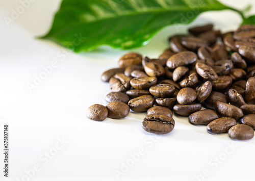 Coffee beans and a leaf of a coffee tree on a white table.Selective focus.