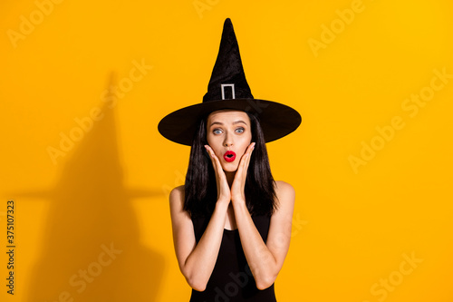 Photo of cute charming young magician lady shocked look hands face see another girl same outfit role play event wear black headwear dress isolated bright yellow color background