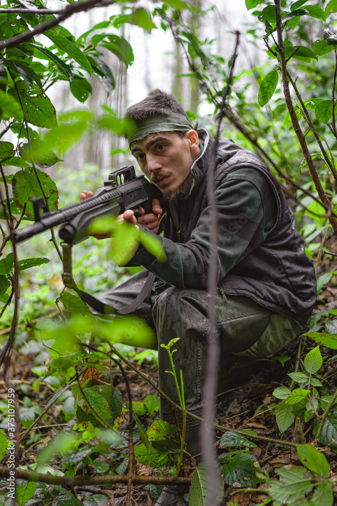 Soldier or revolutionary member or hunter aiming with gun in his hand in camouflage in the forest, hunt concept