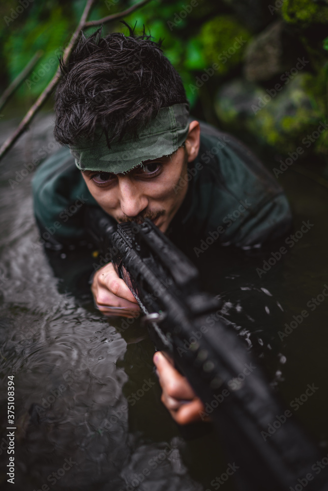 Soldier or revolutionary member or hunter aiming with gun in his hand in camouflage in the river, hunt concept