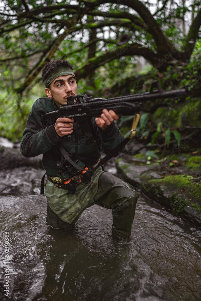 Inside the stream, revolutionary member or hunter in camouflage, gun in his hand, hunting concept