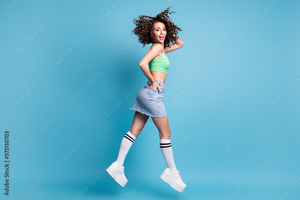 Full length profile side photo of positive cheerful girl jump run want crazy season discounts wear green casual style clothes gumshoes isolated over blue color background