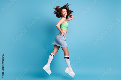Full length profile side photo of positive cheerful girl jump run want crazy season discounts wear green casual style clothes gumshoes isolated over blue color background
