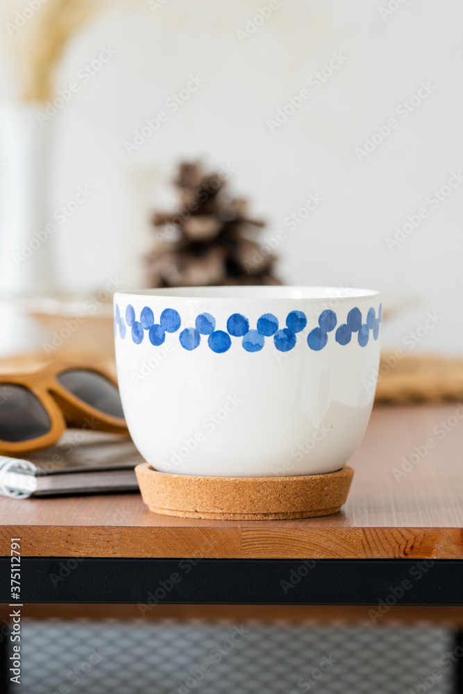 a white mug with a blue pattern, a Notepad and sunglasses on a brown wooden table on a white background. Business lunch. Scandinavian style. a white mug with a blue pattern, a Notepad and sunglasses on a brown wooden table on a white background. Business lunch. Scandinavian style.