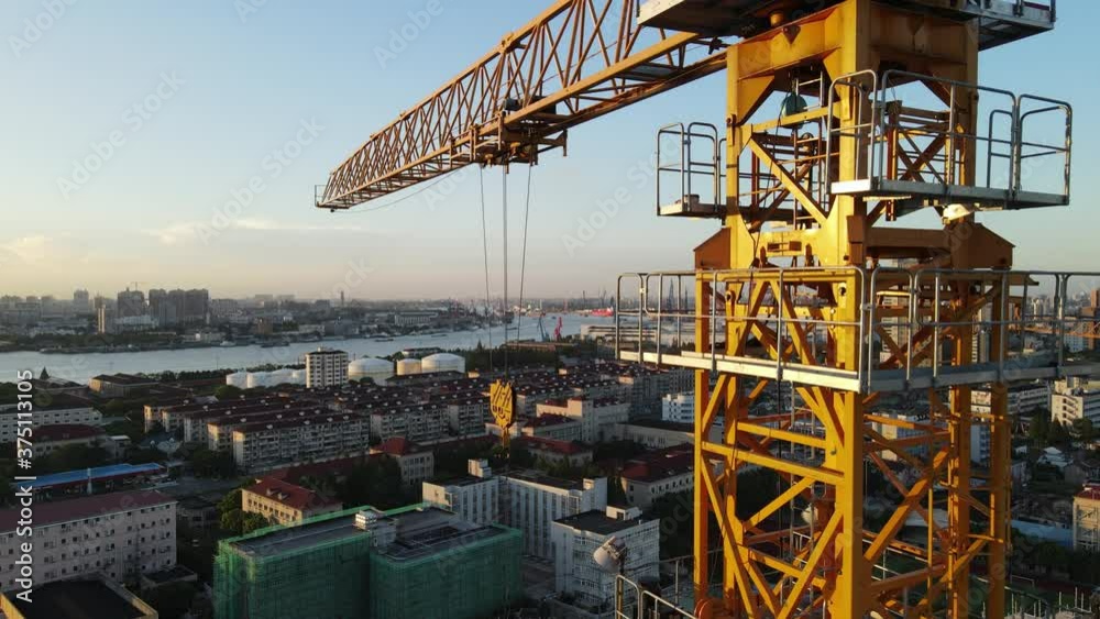 Drone point of view moving up around crane tower in construction site sunset. Close up view of the crane tower lifting material in building site. Industry construction concept footage Shanghai China