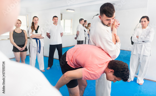 Smiling young coach showing a new submission hold to adults in the taekwondo class