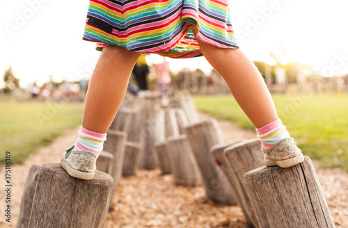 Child does balance exercise on wooden pegs. Little girl balances on logs. Kleines Mädchen balanciert auf Holzstämmen. Kind macht Gleichgewichtsübung auf Holzpflöcken.