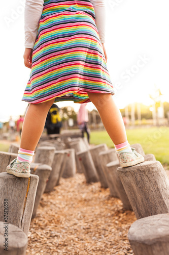 Little girl balances on logs. Child does balance exercise on wooden pegs. Kleines Mädchen balanciert auf Holzstämmen. Kind macht Gleichgewichtsübung auf Holzpflöcken.