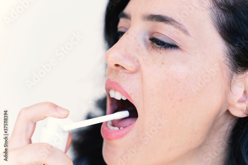 Spray for sore throat. Photo of a woman who treats her throat with a spray and sprinkles it in her mouth. The concept of health and disease.