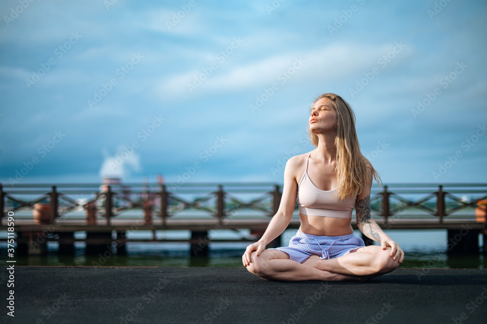 Yoga practice and meditation in nature in sunrise. Woman practicing near City on pier.