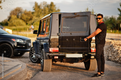 Asian man wear on all black posed near suv car, open rear door.