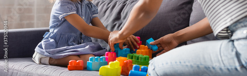 cropped view of african american babysitter and child playing with colorful building blocks on sofa, horizontal image