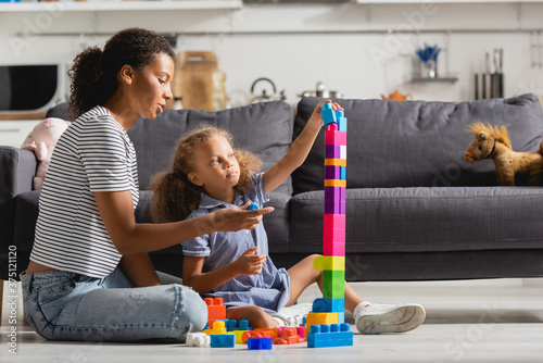 Billede på lærred african american girl building tower from colorful blocks while playing on floor