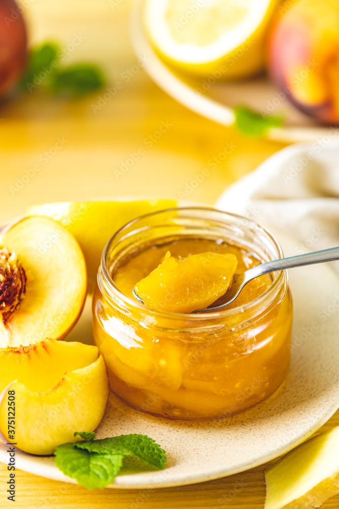Fresh homemade peach jam in glass jar on a wooden background. Several fresh berries, lemon and mint are near it Fresh homemade peach jam in glass jar on a wooden background. Several fresh berries, lemon and mint are near it