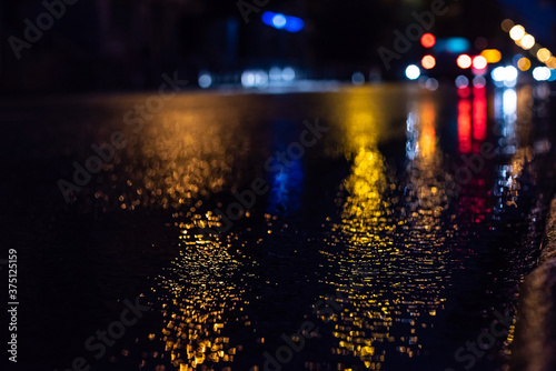 selective focus of city road and car during rain at night, with unfocused lights from headlights of cars. Water from rain and abstract image of side lights in city