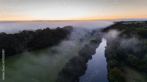 Aerial view of misty morning river during sunrise, rural Ireland landscape.