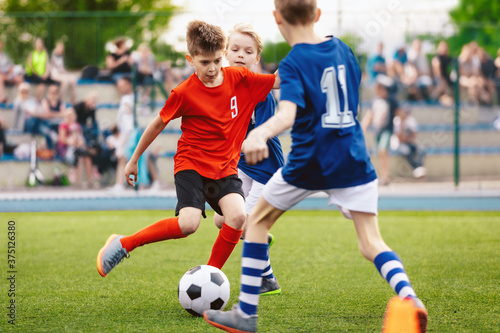 Fototapeta Naklejka Na Ścianę i Meble -  Boys play soccer game. Junior competition between players running and kicking soccer. ball. Youth junior athletes in red and blue soccer shirts. Kids compete in elementary school sports tournament