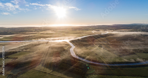 Aerial view of misty morning river during sunrise, rural Ireland landscape.