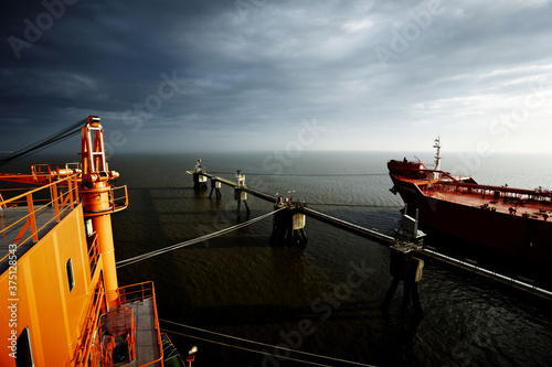 A big oil tanker at dock. Big building at the left and calm weather. Dark, cloudy sky and black water. photo