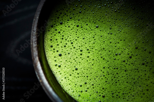 A black bowl of matcha with green foam on top.