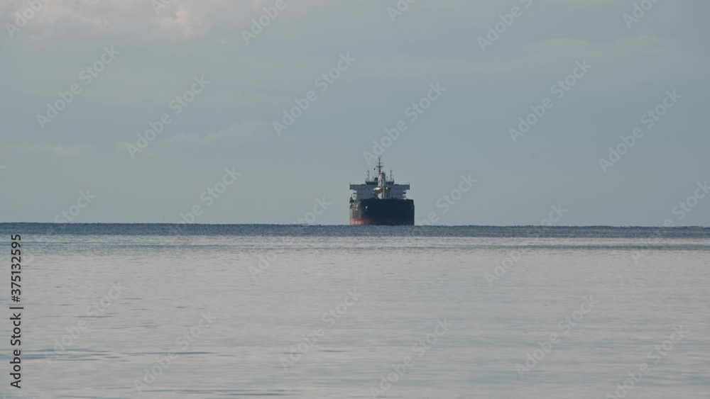Container or cargo ship anchored in the middle outside the bay waiting for unloading. Static, long shot Container or cargo ship anchored in the middle outside the bay waiting for unloading. Static, long shot