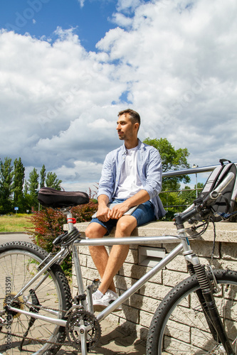 A man sits and holds a laptop. There is a bicycle nearby.