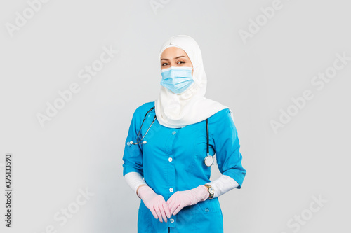  friendly Muslim doctor or nurse wearing hijab and medical face mask and gloves on a gray background.