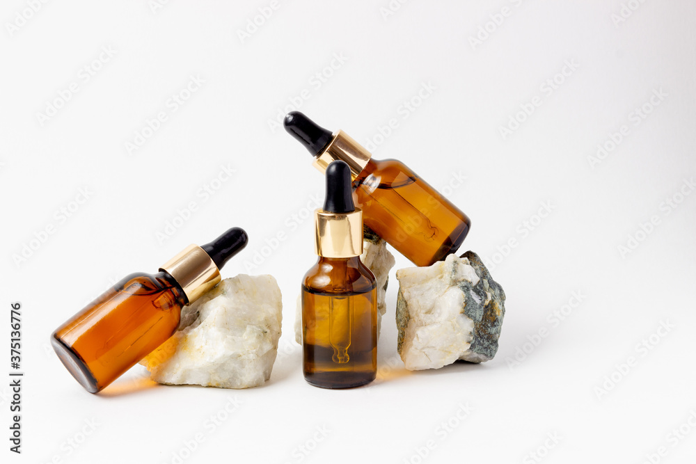 Natural cosmetics in glass bottles with a dropper stand next to a stone on a beige background with bright sunlight. The concept of natural cosmetics, natural essential oil Natural cosmetics in glass bottles with a dropper stand next to a stone on a beige background with bright sunlight. The concept of natural cosmetics, natural essential oil