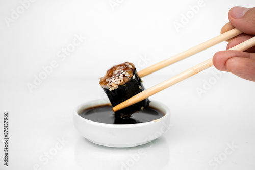 take an unagi maki rolls with bamboo chopsticks and put it into soy sauce on white background, asian food, japanese cuisine