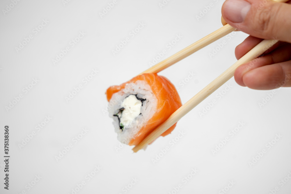 take a philadelphia maki rolls with bamboo chopsticks and put in into soy sauce. pink ginger, wasabi on white plate, asian food, japanese cuisine background take a philadelphia maki rolls with bamboo chopsticks and put in into soy sauce. pink ginger, wasabi on white plate, asian food, japanese cuisine background