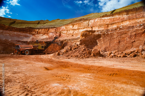Aluminium ore mining and transporting. Bauxite clay. Excavator loads an ore to Hitachi dump truck. Blue sky with light clouds.