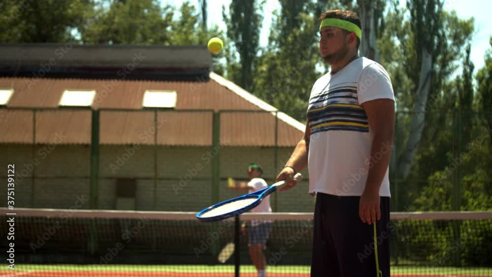 Plump sportsman juggling tennis ball on racket Plump sportsman juggling tennis ball on racket