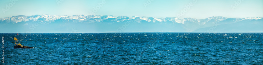 Panorama of blue water of Lake Baikal, with mountain peaks against the sky with a tree in the middle of summer