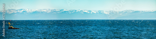 Panorama of blue water of Lake Baikal  with mountain peaks against the sky with a tree in the middle of summer