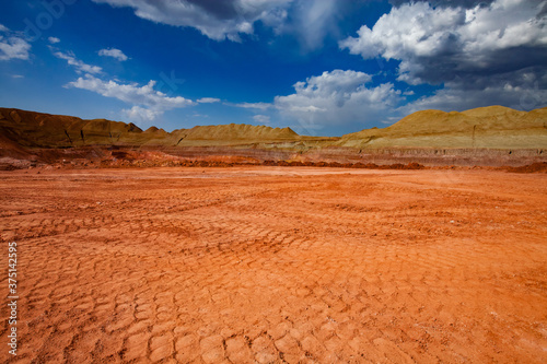 Aluminium ore quarry. Bauxite clay open-cut mining. Truck trails on the ground. Green grass on the heaps. Blue sky with clouds. Panoramic view.