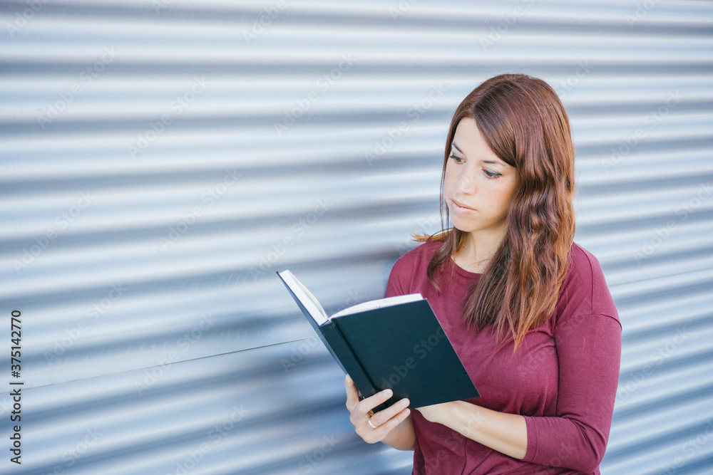Fototapeta premium young girl reading at a cover black book on the street