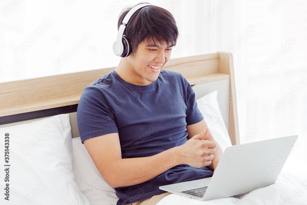 Happy Asian man using Laptop computer and checking good News in the Bedroom. COPY SPACE. Trading. Watching Movie. WORK FROM HOME Concept. New Normal Concept. Happy Asian man using Laptop computer and checking good News in the Bedroom. COPY SPACE. Trading. Watching Movie. WORK FROM HOME Concept. New Normal Concept.