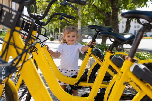 Wallpaper Mural little girl is standing next to bicycle to rent in the parking lot in the city. Torontodigital.ca