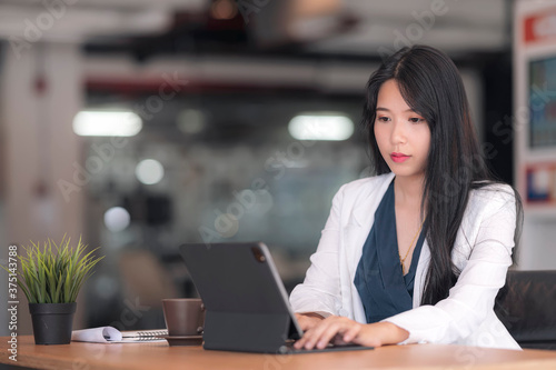 Young beautiful asian businesswoman working with tablet computer while sitting in contemporary office room.