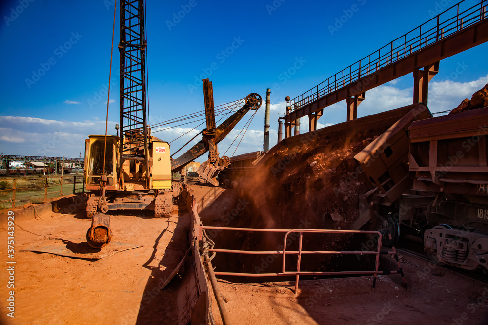 Bauxite clay open-cut mining. Loading and railway transporting terminal. Excavator loading aluminium ore from train on rails.