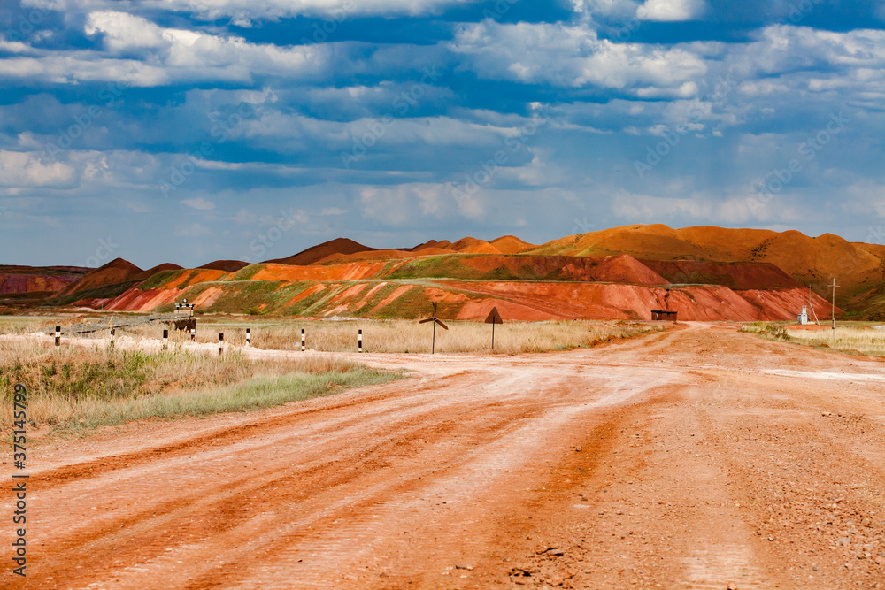 Landscape of bauxite mine (aluminium ore quarry). Orange clay soil and blue sky with clouds. Dump heaps and road with road signs. Blue sky with cloud.