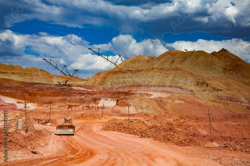 Aluminium ore quarry. Bauxite clay open-cut mining. Walking dragline excavators on heap of ground and bulldozer on road. Blue sky with clouds.