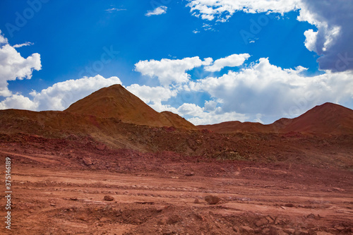 Aluminium ore quarry. Bauxite clay open-cut mining. Heaps of empty rocks. Blue sky with clouds and road.